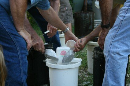 People hand scoop and pack ice and food into a white bucket outdoors.